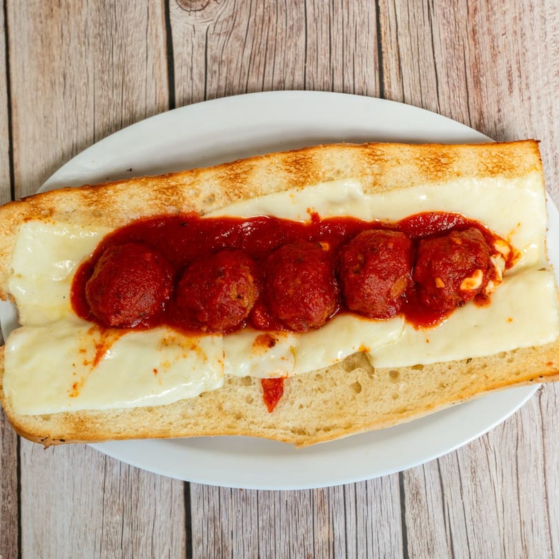 RigaTony's meatball sub with melted mozzarella cheese and marinara sauce on a white plate.