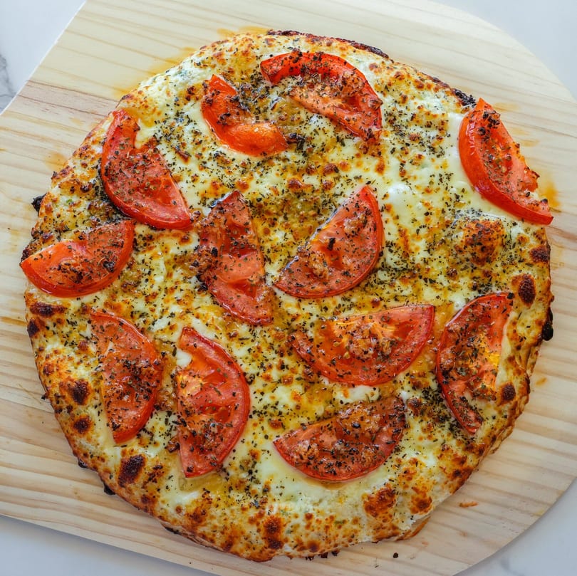 RigaTony's Pizza & Pasta's cheesy pizza with sliced tomatoes and herbs on a wooden peel.