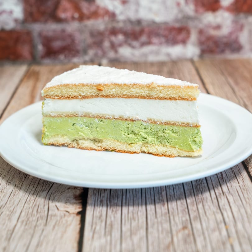 A slice of layered cake with white and green filling, dusted with powdered sugar, on a white plate.