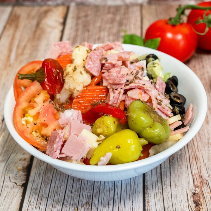 RigaTony's antipasto salad with salami, ham, cheese, tomatoes, olives, and peppers in a white bowl.