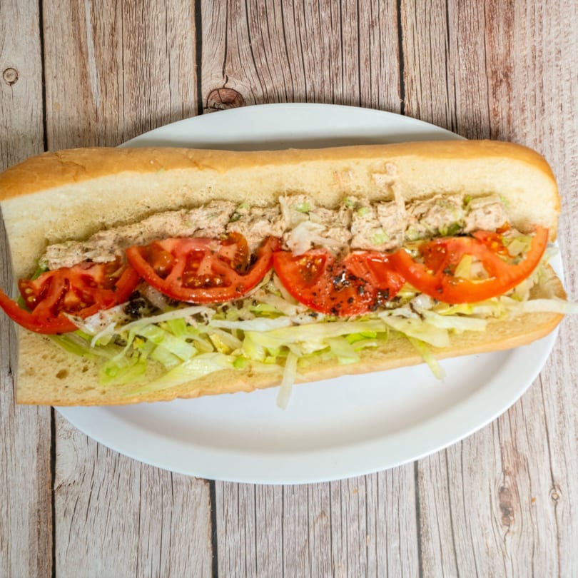 A long tuna sub sandwich with lettuce and tomatoes on a white plate.