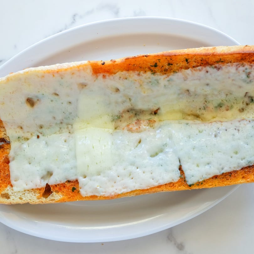 RigaTony's cheesy garlic bread, a long toasted baguette covered in melted white cheese and herbs.